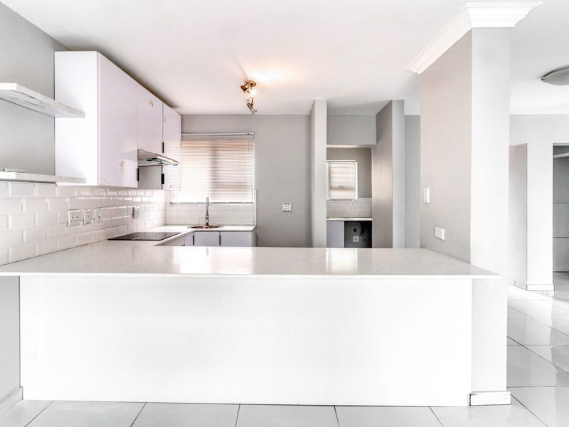 Modern kitchen featuring white cabinetry, quartz countertops, subway tile backsplash, and an integrated hob, with an adjacent scullery area and tiled flooring.