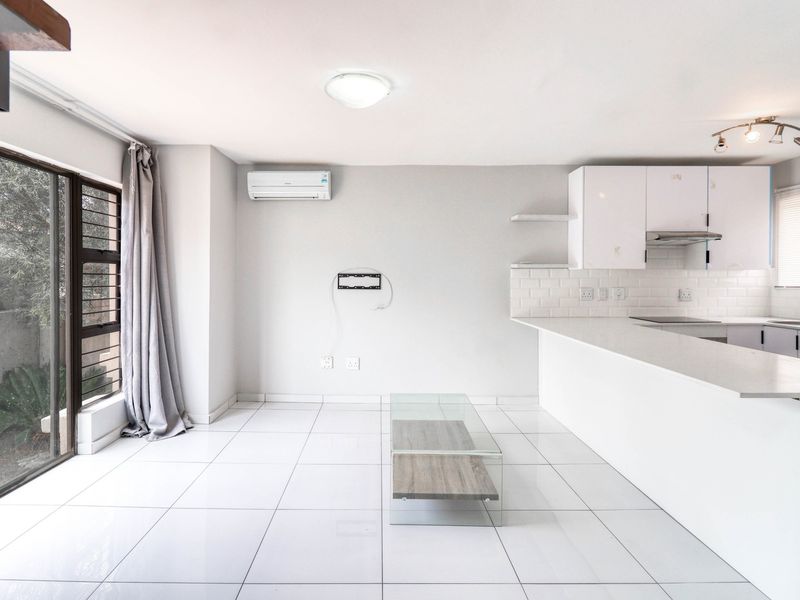 Bright open-plan living and kitchen area featuring white cabinetry, stone countertops, subway tile backsplash, air conditioning, and large sliding doors leading to the exterior.