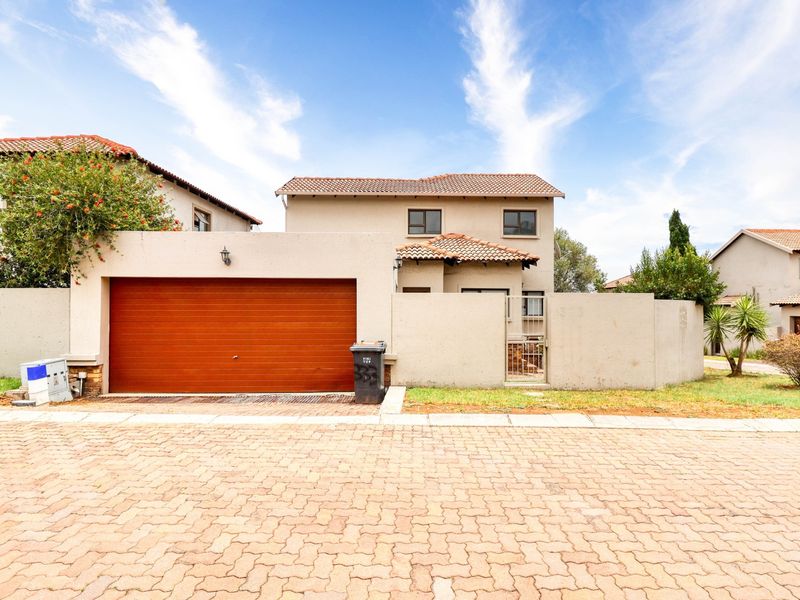 Front elevation of a cluster home featuring a tiled roof, automated garage door, and a paved driveway with a secure pedestrian entrance.