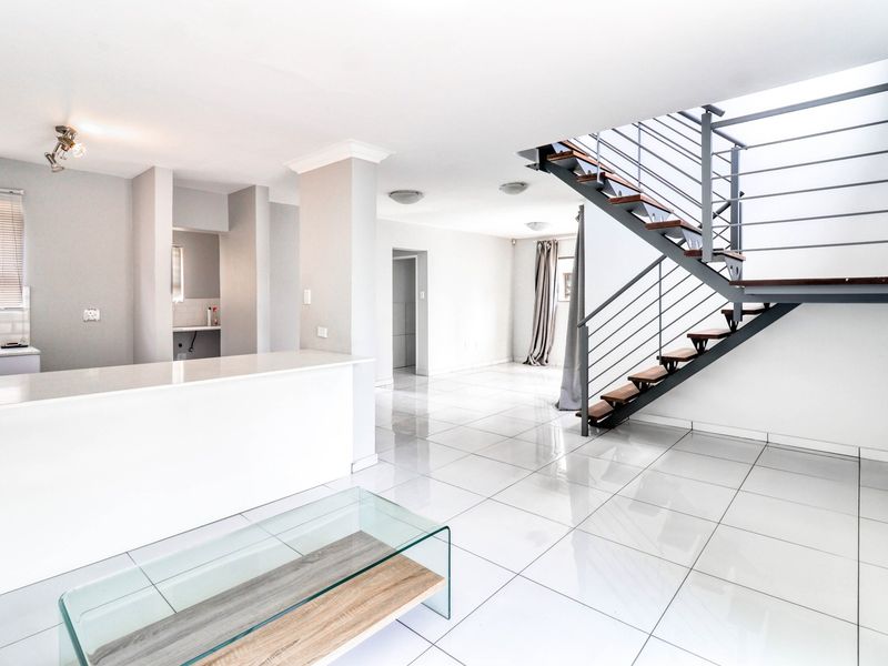 Spacious open-plan living area featuring modern tiled flooring, a central kitchen island, and a contemporary staircase with metal railings.
