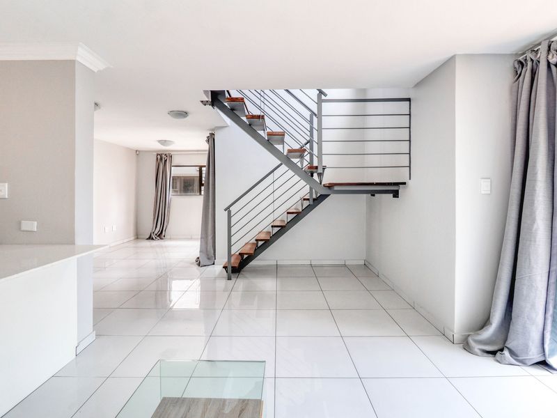 Spacious open-plan living area featuring modern tiled flooring and a contemporary staircase with a metal balustrade.