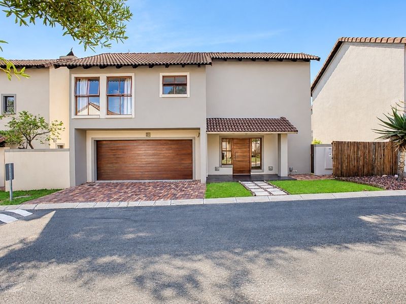 A well-maintained double-story townhouse featuring a paved driveway, wooden garage door, and a welcoming entrance with a timber front door.
