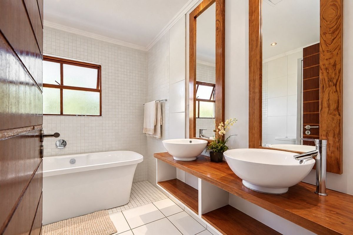 Modern bathroom featuring a freestanding bathtub, double vessel sinks on a wooden vanity, and elegant mosaic wall tiling.