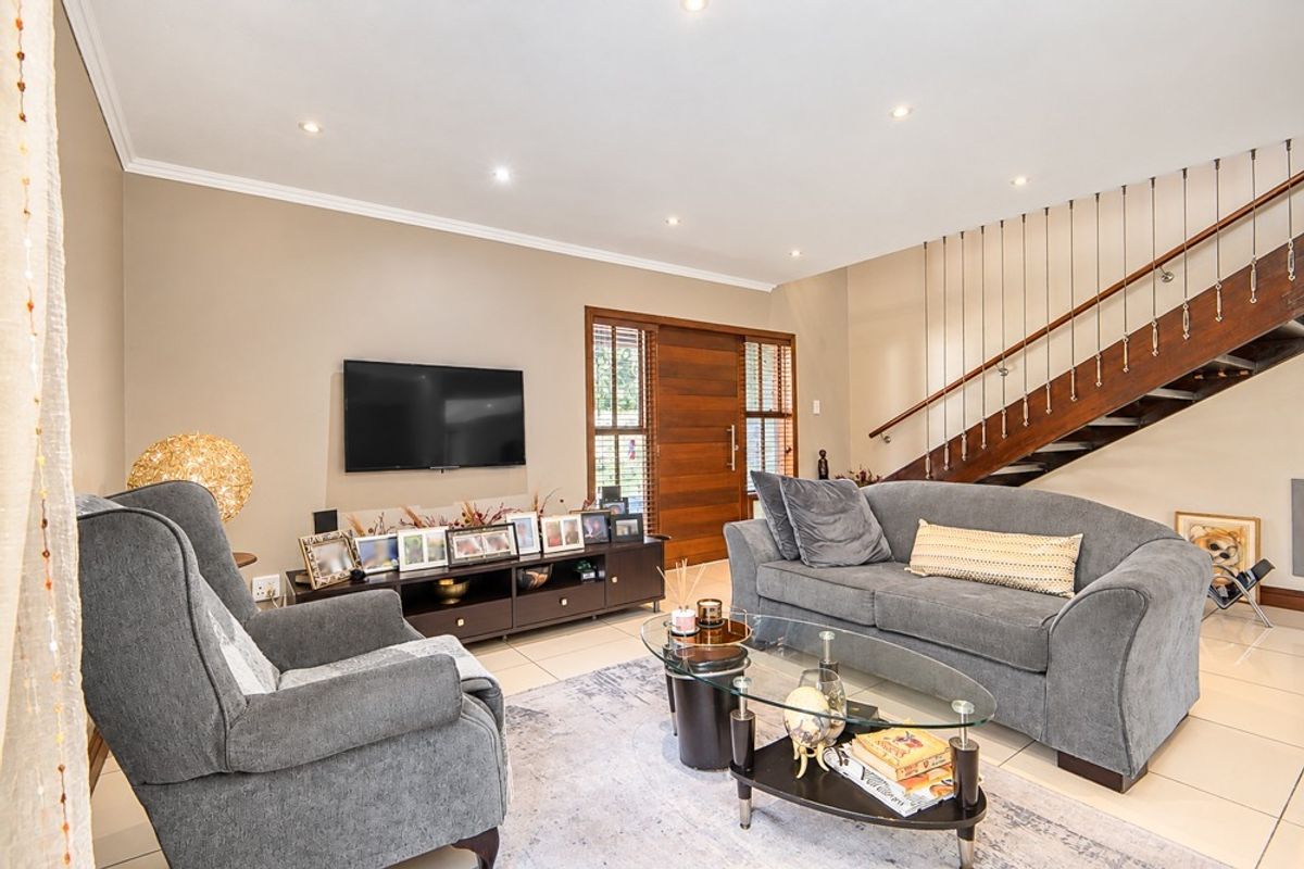 A well-maintained living room featuring tiled flooring, recessed downlights, and an elegant wooden staircase with a modern metal balustrade.