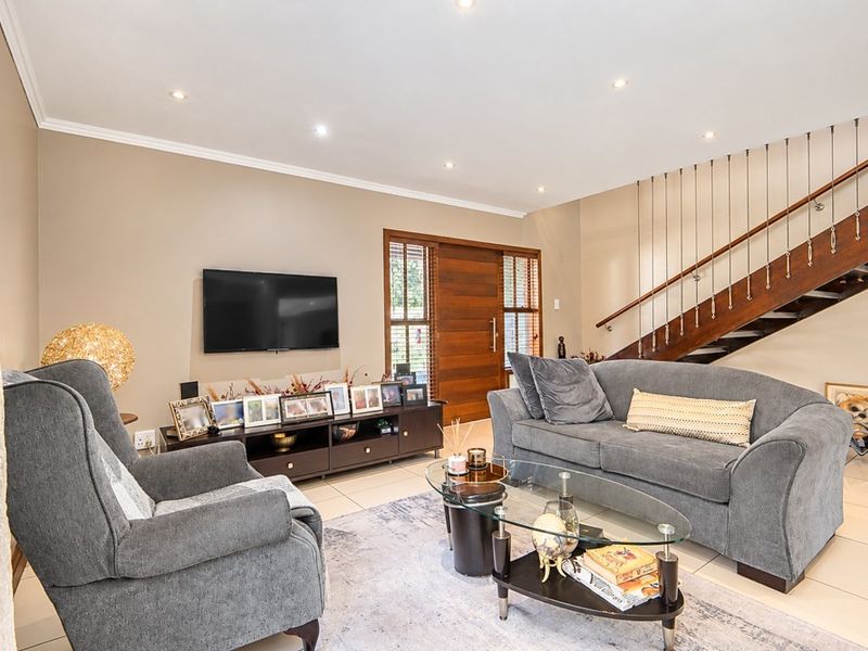 A well-maintained living room featuring tiled flooring, recessed downlights, and an elegant wooden staircase with a modern metal balustrade.