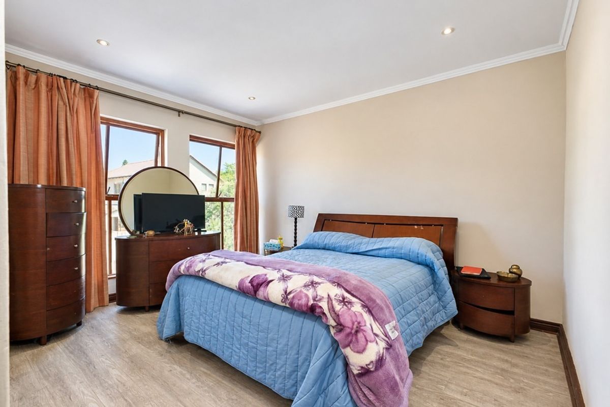 A well-lit bedroom featuring laminate flooring, recessed downlighting, and large windows that provide natural light.