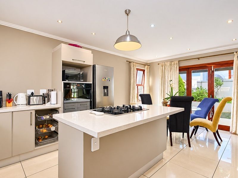 Modern open-plan kitchen featuring a central island with a gas hob, stone countertops, built-in appliances, and direct access to the outdoor patio area.