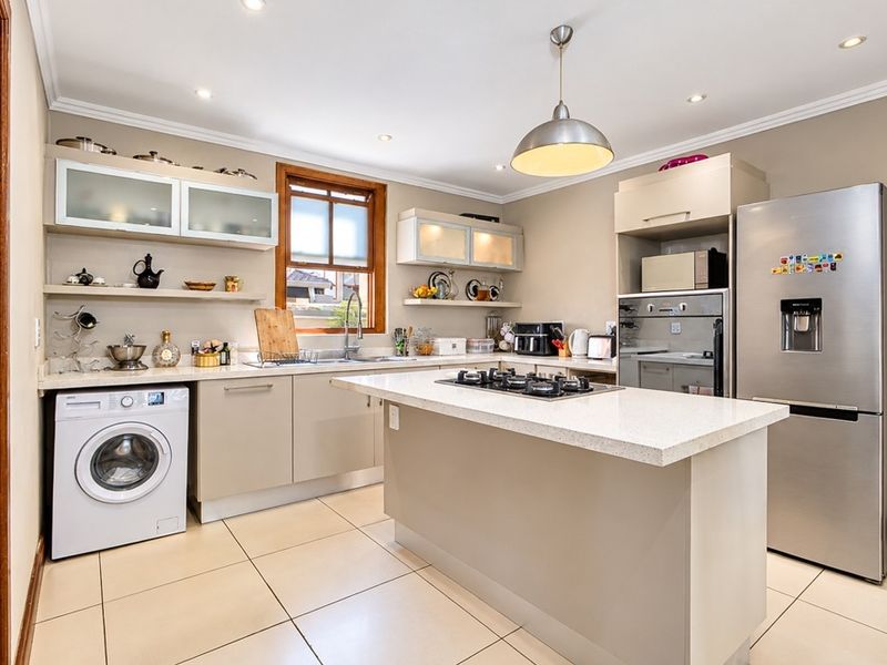 Modern kitchen featuring stone countertops, a central island with a gas hob, built-in oven, and integrated cabinetry with ample storage space.