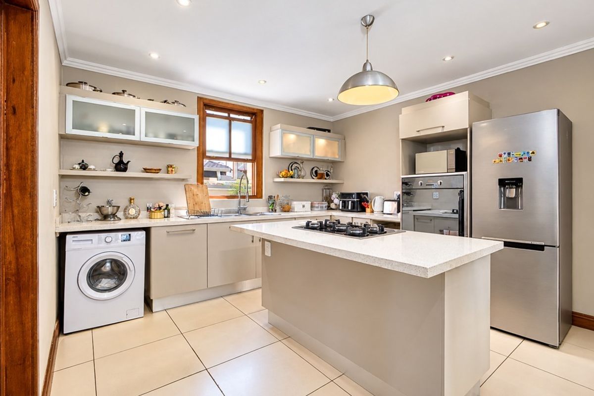 Modern kitchen featuring stone countertops, a central island with a gas hob, built-in oven, and integrated cabinetry with ample storage space.