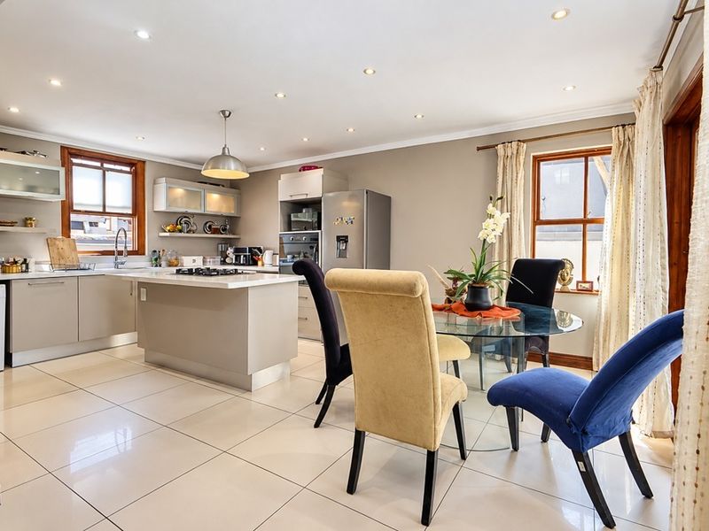 Open-plan kitchen and dining area featuring a central island, modern cabinetry, built-in appliances, and polished tiled flooring with recessed lighting.