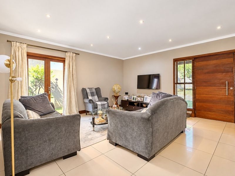 A bright and spacious living room featuring large format floor tiles, recessed downlighting, and direct access to the garden through wooden framed glass doors.