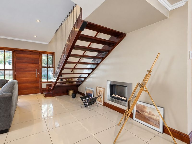 Spacious living area featuring polished porcelain tiles, a striking open-tread timber staircase with cable balustrade, and a modern built-in gas fireplace.