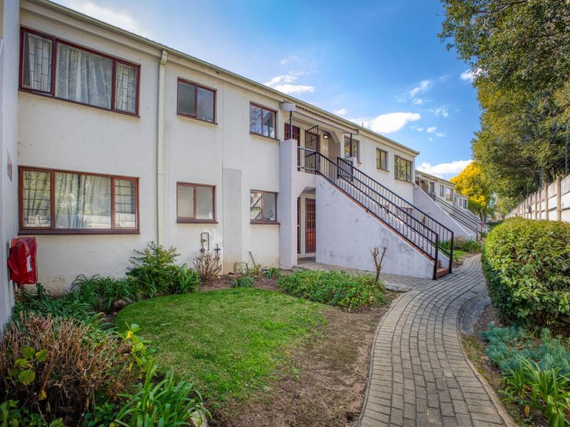 Exterior view of an apartment complex featuring a paved walkway, landscaped garden, and external staircases leading to upper-level units.