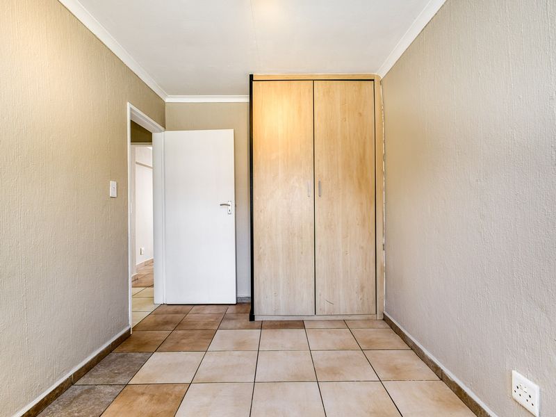 A clean, empty hallway featuring neutral tiled flooring, coving, and a built-in wooden cupboard, providing a functional transition space within the apartment.