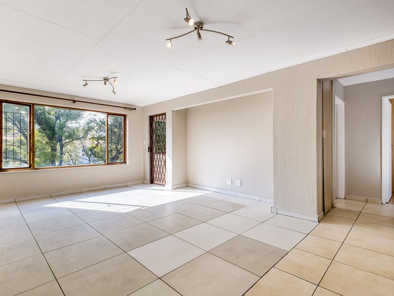 A bright and spacious empty living area featuring neutral tiled flooring, large windows, and a security gate, offering a clean canvas for personalization.