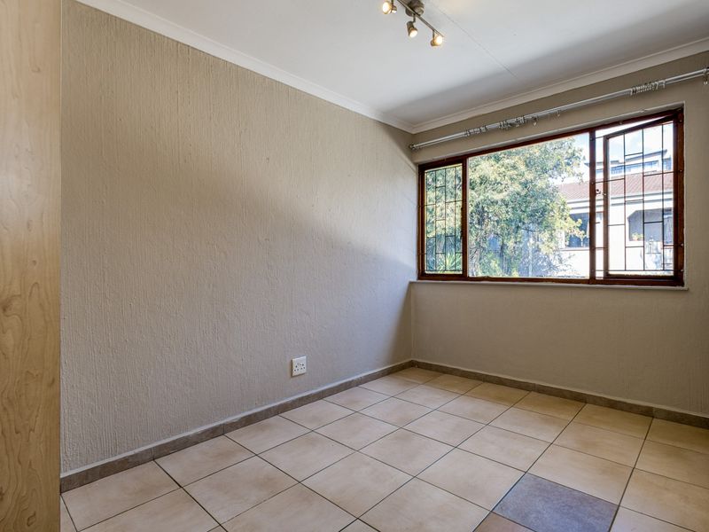 A vacant bedroom featuring tiled flooring, textured walls, a built-in cupboard, and a window fitted with security bars.