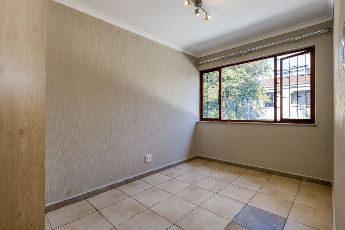 A vacant bedroom featuring tiled flooring, textured walls, a built-in cupboard, and a window fitted with security bars.