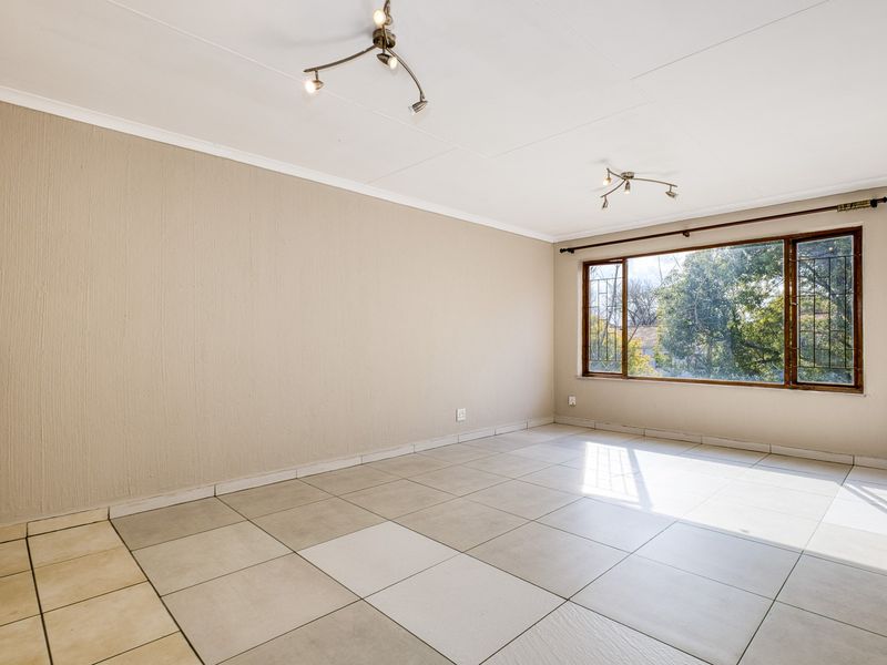 A spacious, empty living room featuring neutral textured walls, large windows with security bars, and tiled flooring throughout.