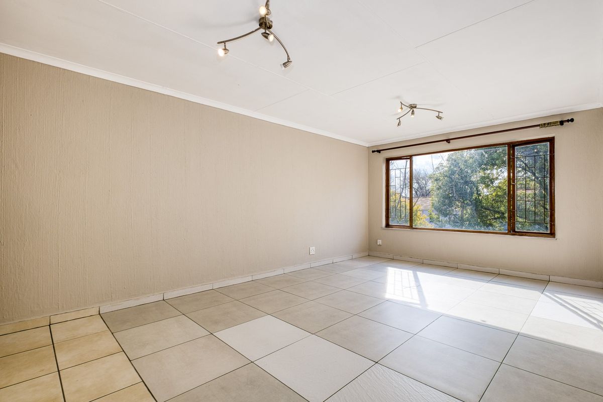 A spacious, empty living room featuring neutral textured walls, large windows with security bars, and tiled flooring throughout.