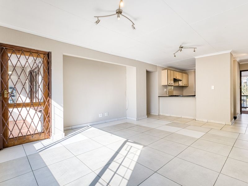 Spacious open-plan living area featuring tiled flooring, a security gate, and a functional kitchen with built-in cabinetry and integrated appliances.