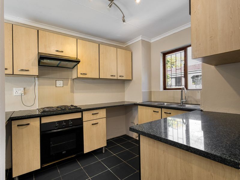 Functional kitchen featuring light wood cabinetry, dark granite countertops, built-in oven and hob, and tiled flooring with a window overlooking the exterior.