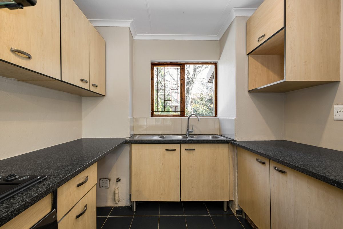 A functional kitchen featuring light wood-finish cabinetry, dark countertops, a double sink, and tiled flooring, offering a clean space ready for updates.