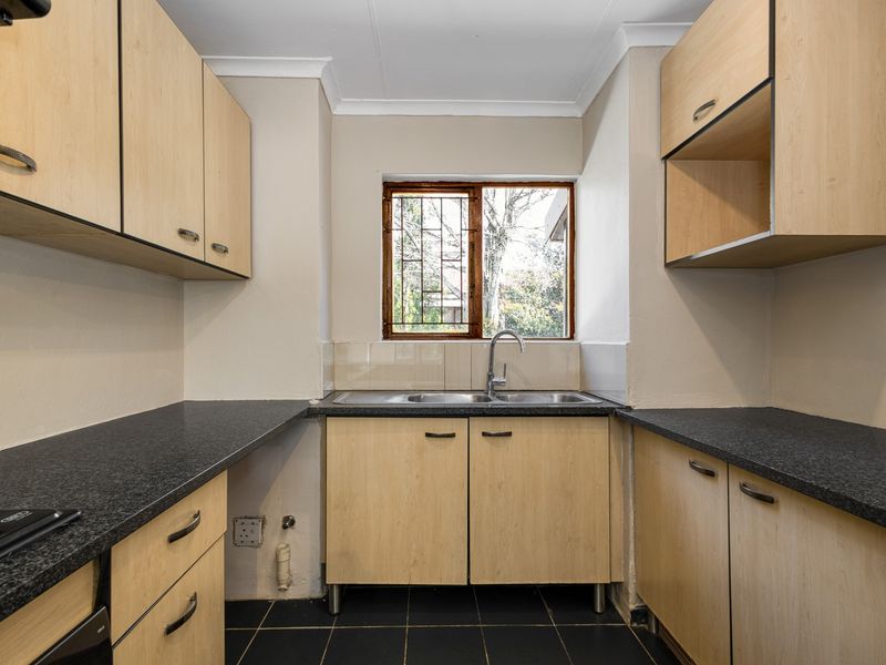 A functional kitchen featuring light wood-finish cabinetry, dark countertops, a double sink, and tiled flooring, offering a clean space ready for updates.