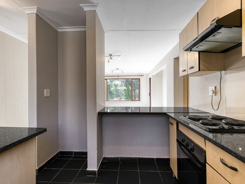Open-plan kitchen featuring granite countertops, built-in oven, electric hob, and extractor fan, flowing into a bright living area with tiled flooring throughout.
