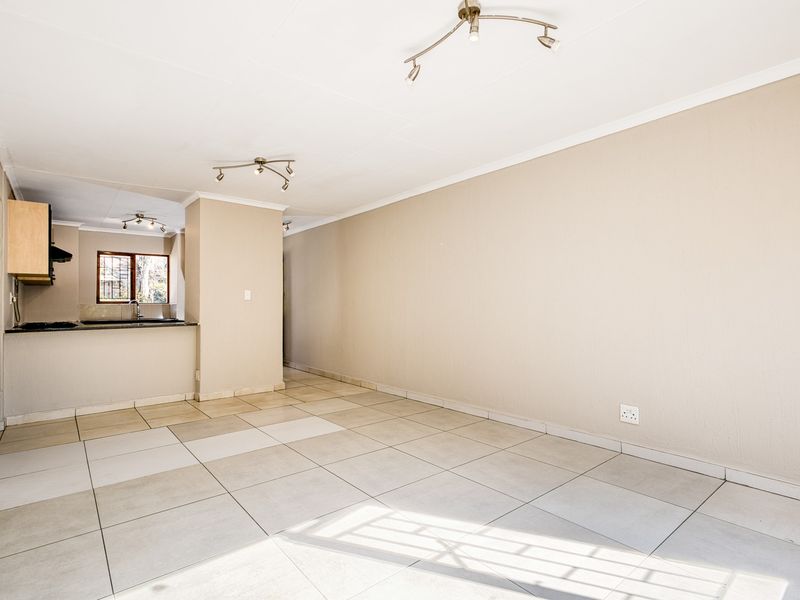 An open-plan living and kitchen area featuring neutral tiled flooring, ample wall space, and functional kitchen cabinetry with a breakfast counter.