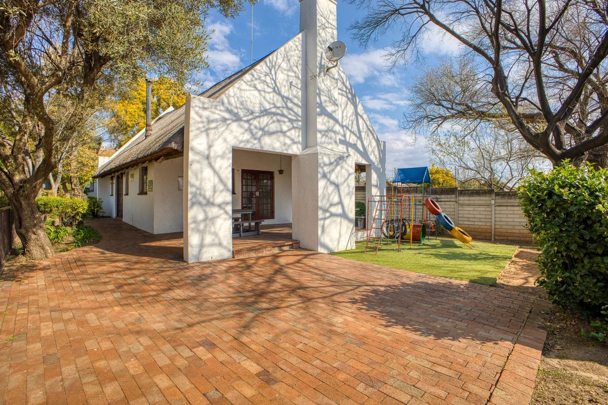 Rear view of a property featuring a thatched roof, a brick-paved patio area, and a private garden space with a boundary wall.