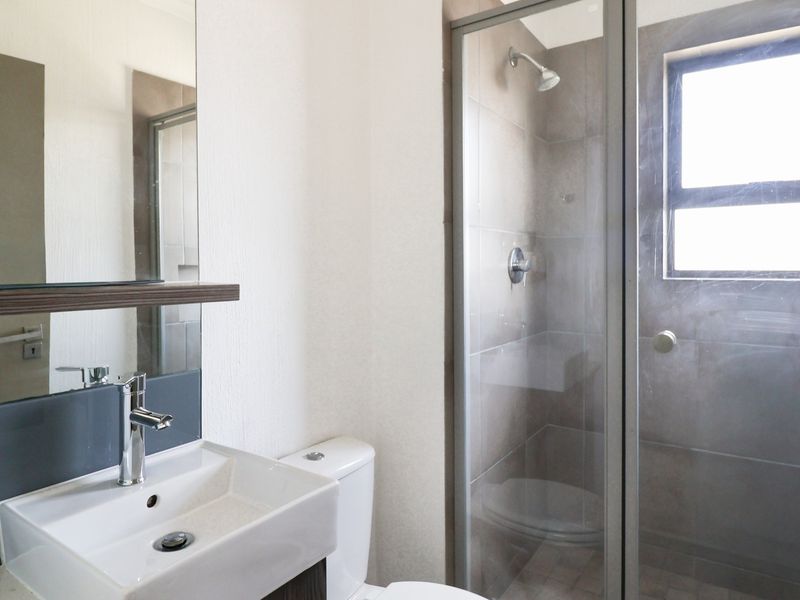 A clean, modern bathroom featuring a vanity basin, toilet, and a glass-enclosed shower with tiled walls and natural light.