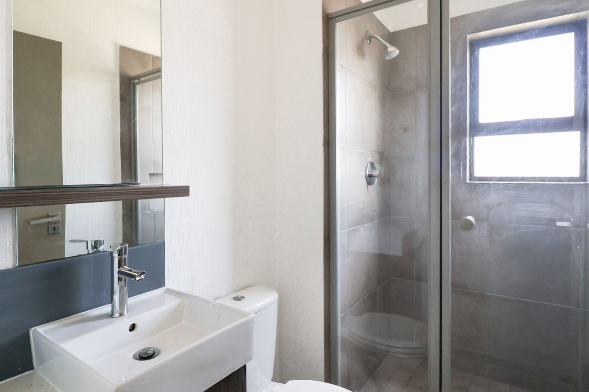 A clean, modern bathroom featuring a vanity basin, toilet, and a glass-enclosed shower with tiled walls and natural light.