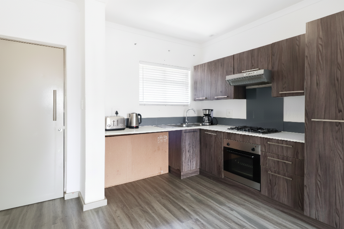 A functional kitchen featuring dark wood-grain cabinetry, a gas hob, built-in oven, and modern laminate flooring, though one lower cabinet door is currently missing.