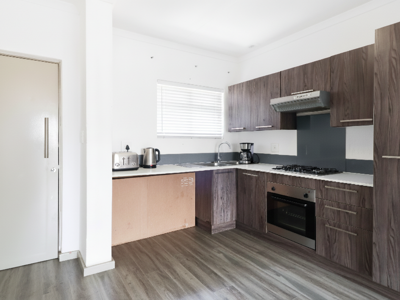 A functional kitchen featuring dark wood-grain cabinetry, a gas hob, built-in oven, and modern laminate flooring, though one lower cabinet door is currently missing.