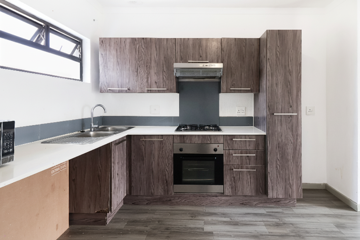 Modern kitchen featuring wood-grain cabinetry, stone countertops, integrated gas hob, oven, and extractor fan, with durable laminate flooring throughout.
