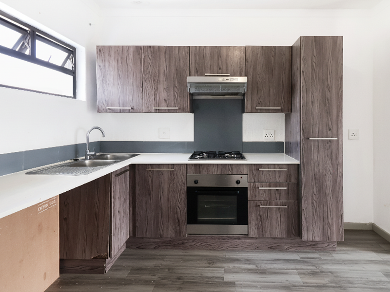 Modern kitchen featuring wood-grain cabinetry, stone countertops, integrated gas hob, oven, and extractor fan, with durable laminate flooring throughout.