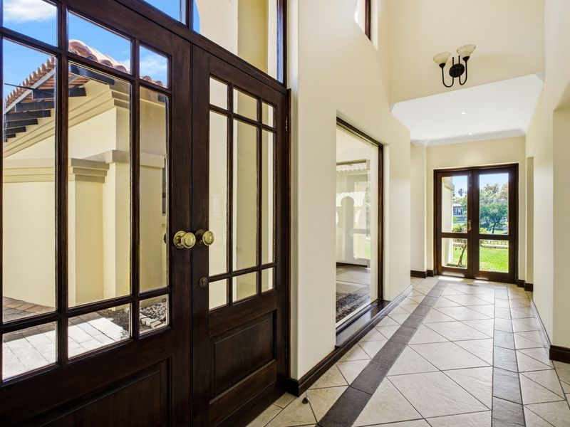 Spacious and bright entrance hall featuring high ceilings, elegant tiled flooring with a decorative border, and large glass doors providing natural light.