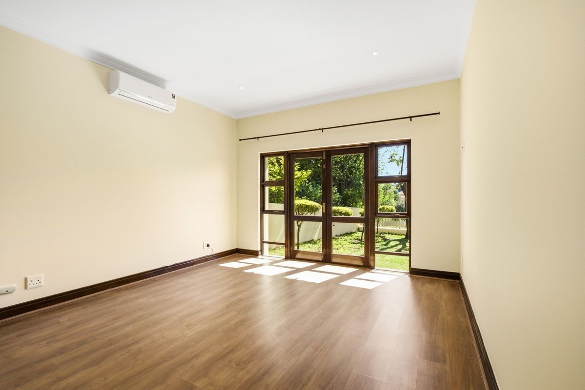 A bright, empty bedroom featuring laminate flooring, air conditioning, and timber-framed glass doors providing direct access to the garden.