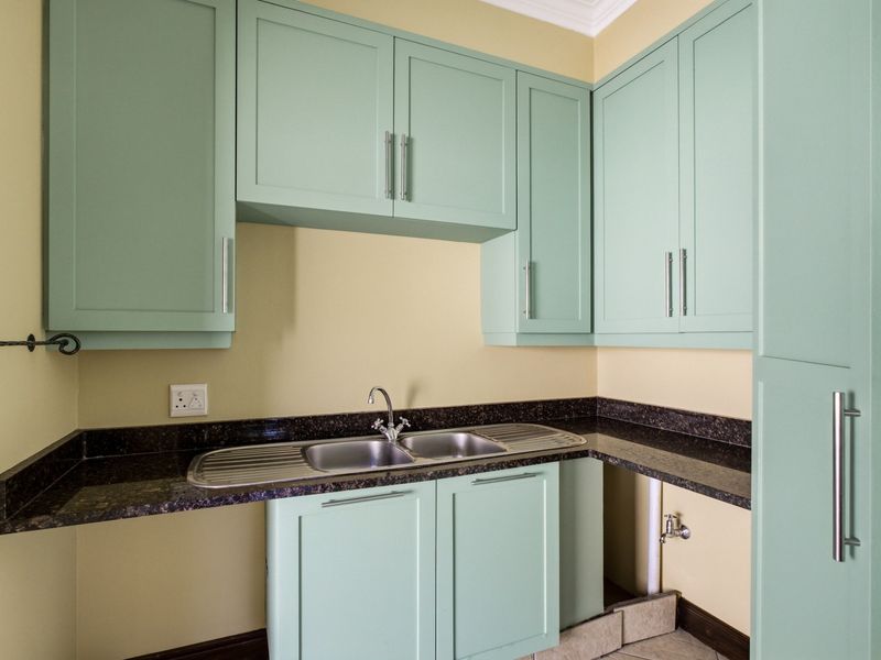 A functional scullery area featuring mint green cabinetry, granite countertops, and a double stainless steel sink with dedicated plumbing connections.