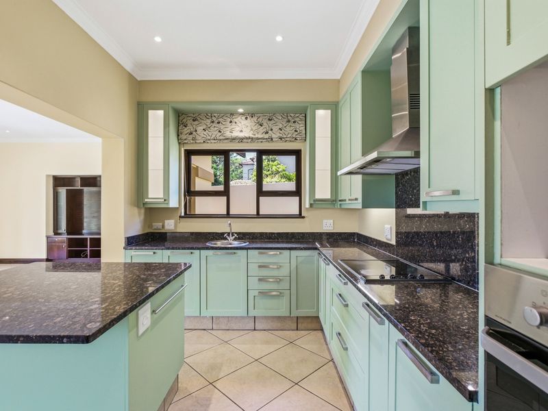 A well-maintained kitchen featuring light green cabinetry, dark granite countertops, built-in appliances, and tiled flooring, offering a clean and functional workspace.