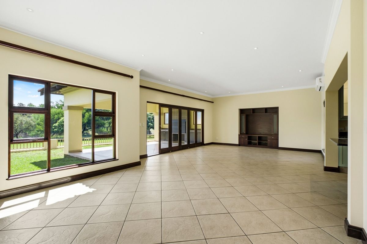 Spacious, light-filled living area featuring neutral tiled floors, recessed lighting, a built-in media unit, and large sliding doors opening to the outdoor patio.