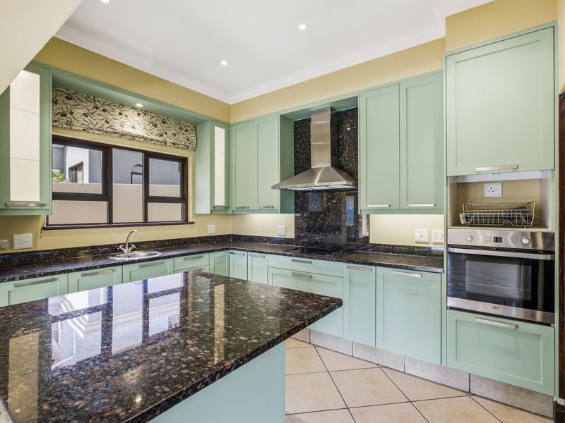 A well-maintained kitchen featuring light green cabinetry, dark granite countertops, built-in oven, extractor fan, and tiled flooring.