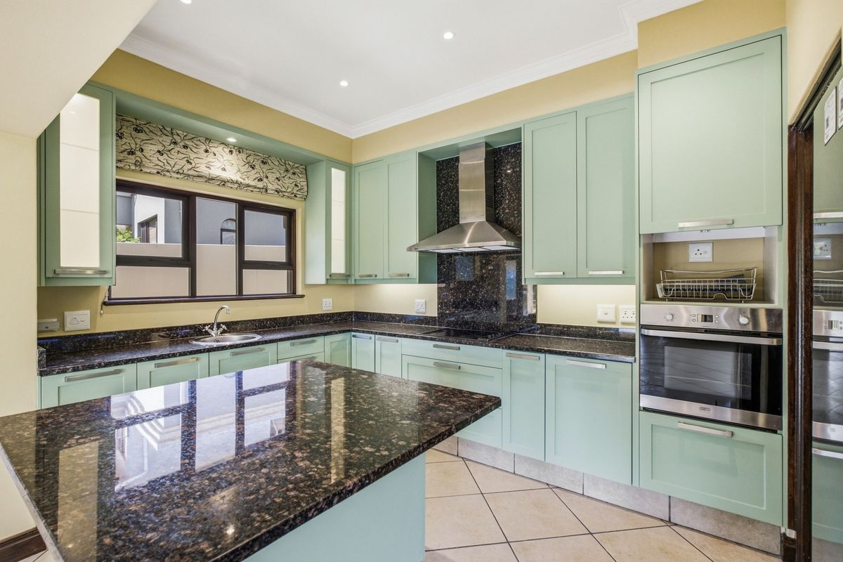 A well-maintained kitchen featuring light green cabinetry, dark granite countertops, built-in oven, extractor fan, and tiled flooring.