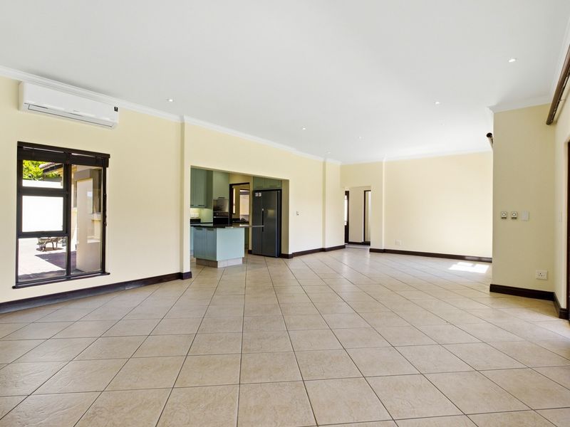 Spacious open-plan living area featuring neutral tiled flooring, recessed lighting, and a wall-mounted air conditioning unit, with an adjacent kitchen area.