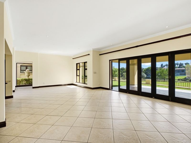 Spacious, light-filled living area featuring neutral tiled floors, recessed lighting, and large aluminium stacking doors that open onto a patio with garden views.