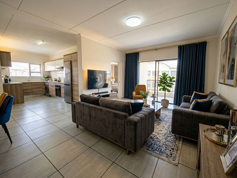 Spacious open-plan living area featuring modern tiled floors, a contemporary kitchen with built-in cabinetry, and seamless access to a private balcony.