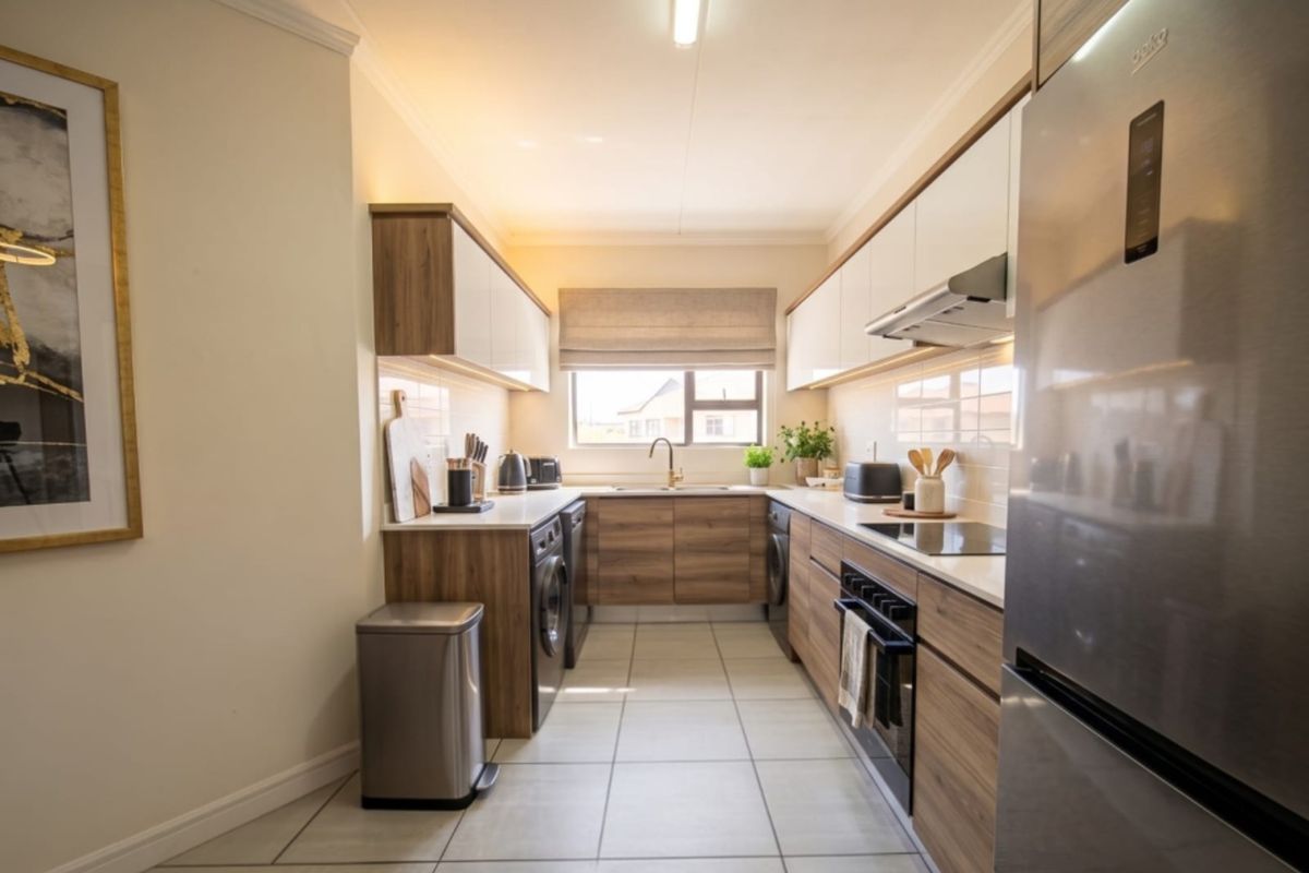 A modern, well-appointed galley kitchen featuring wood-grain cabinetry, stone countertops, integrated appliances, and sleek tiled flooring with ample under-cabinet lighting.