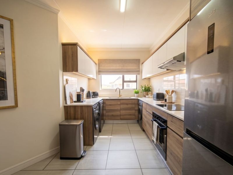 A modern, well-appointed galley kitchen featuring wood-grain cabinetry, stone countertops, integrated appliances, and sleek tiled flooring with ample under-cabinet lighting.