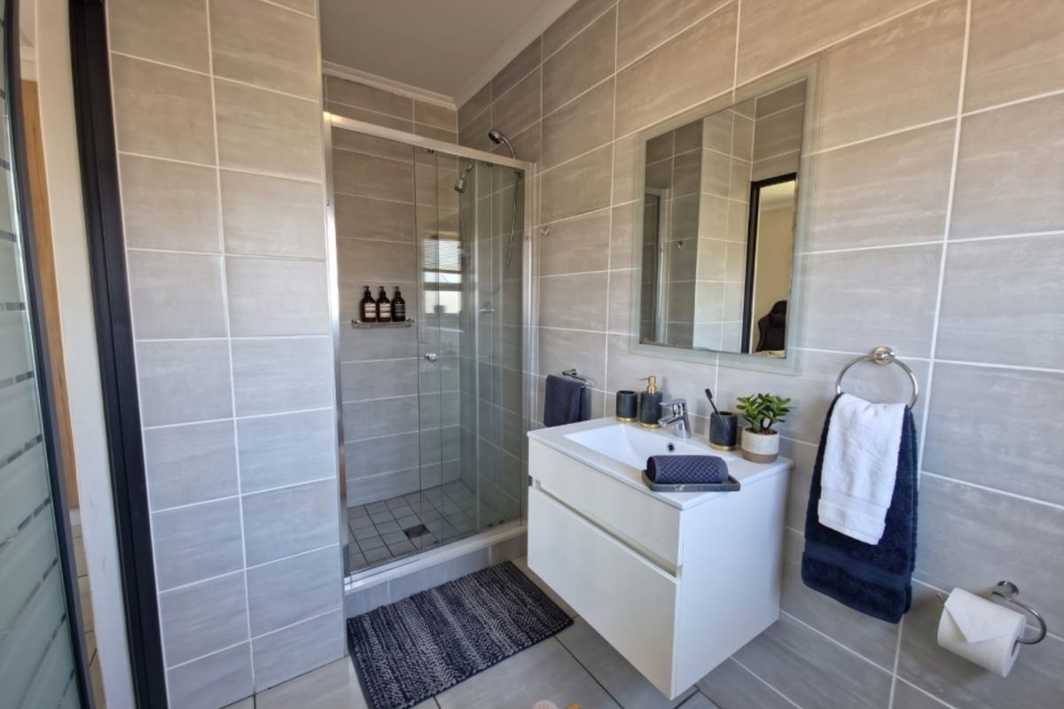 Modern bathroom featuring a walk-in glass shower, wall-mounted vanity with integrated basin, and neutral floor-to-ceiling tiling.