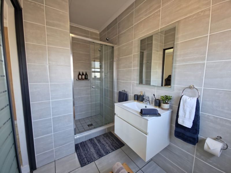 Modern bathroom featuring a walk-in glass shower, wall-mounted vanity with integrated basin, and neutral floor-to-ceiling tiling.